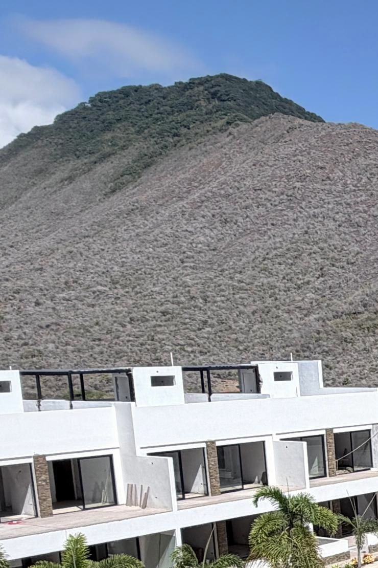 Módulos blancos de Los Geckos con detalles de piedra y palmas, al pie del cerro. Foto de obra · octubre 2026.