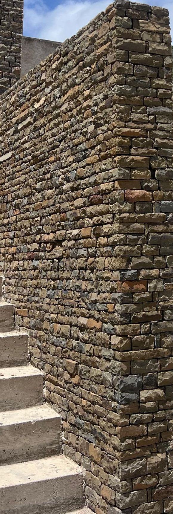 Muro de piedra seca de Los Geckos al lado de una escalera, con el cerro verde al fondo. Los Geckos · foto de obra.